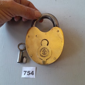May include: A vintage brass padlock and key. The padlock has a heart-shaped body and a circular handle. The key is small and silver. The padlock is inscribed with "HERM. RUBENS SOHN ELBERFELD".