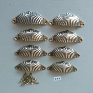 May include: Eight silver-toned cabinet knobs with a fluted design. The knobs are arranged in two rows of four. A small pile of screws is in the lower left corner of the image. The number 671 is written in black on a white background in the lower center of the image.