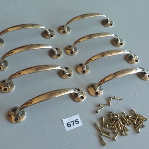 May include: Eight polished brass cabinet handles with matching screws. The handles have a curved design and are mounted on round bases. The image shows a set of hardware for furniture restoration or new construction projects.