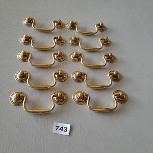 May include: Twelve gold-toned drawer pulls with a simple, elegant design. Each pull has a rounded, slightly raised center and a smooth, curved handle.