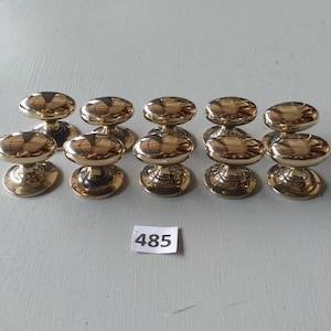 May include: A collection of ten polished brass cabinet knobs. Each knob has an oval handle and a round base. The knobs are arranged in two rows on a light gray surface. The number "485" is printed on a white label.