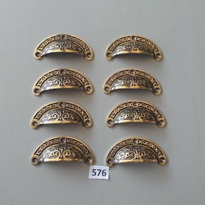 May include: Eight antique brass cabinet pulls with an ornate design. The pulls are half-round and have a decorative floral pattern.