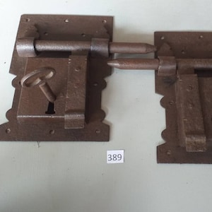 May include: Two antique iron door locks with keys. The locks are rectangular and have a decorative design around the edges. The locks are rusty and have a dark brown colour. The number 389 is written on a white label below the locks.