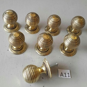 May include: A collection of eight brass door knobs. Each knob features a spherical design with concentric ridges, mounted on a circular base. One knob is detached, showing the screw. The knobs have a polished, golden finish.