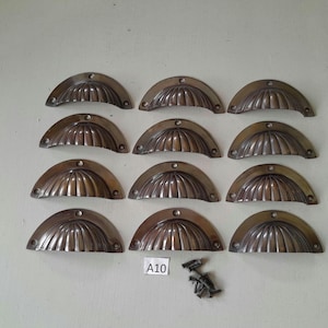 May include: A set of 10 antique brass cabinet pulls with a scalloped design. The pulls are arranged in two rows of five, with the text "A10" visible in the lower right corner of the image.