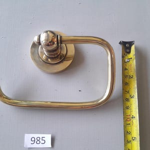 May include: A gold-toned toilet paper holder with a round base and a curved arm. The holder is 4 inches tall.