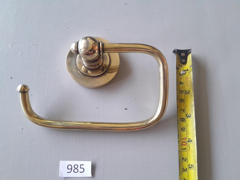 May include: A gold-toned toilet paper holder with a round base and a curved arm. The holder is 4 inches tall.