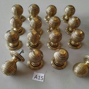 May include: A collection of 15 brass door knobs with a ribbed design. The knobs are arranged in a semi-circle on a light gray surface. The knobs are all the same size and shape, and they have a shiny finish.