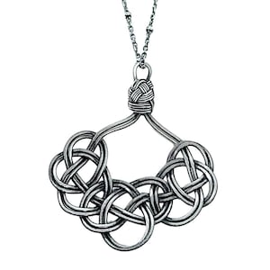 Op de afbeelding: Een zilveren ketting met een grote, ingewikkelde knoop hanger. De hanger is gemaakt van meerdere verweven metalen strengen, wat resulteert in een complex en elegant ontwerp.