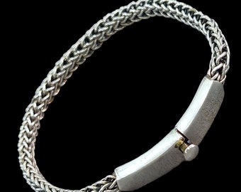 Op de afbeelding: Een zilveren kettingarmband met een zilveren sluiting. De armband is gemaakt van een geweven kettingpatroon.