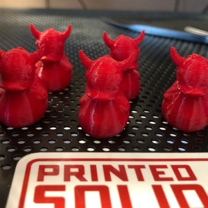 May include: Five red rubber duck figurines with horns and helmets. The ducks are sitting on a black surface with a circular pattern.