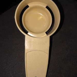May include: A beige plastic egg separator with a handle and the word "Tupperware" printed on the side.