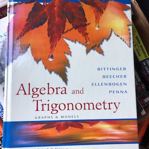 Puede incluir: Un libro de texto de tapa dura titulado Algebra and Trigonometry Graphs & Models Third Edition por Bittinger, Beecher, Ellenbogen y Penna. La cubierta blanca presenta un gráfico grande de una hoja de arce naranja y roja.
