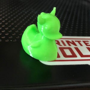 May include: A bright green 3D printed figurine of a unicorn with a horn, a small tail, and a rounded body.