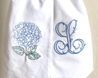 May include: White fabric sash with blue embroidered hydrangea flower and a blue embroidered letter L.