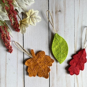 May include: Three felt leaf ornaments in orange, green, and red. Each leaf has a string for hanging.