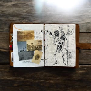 May include: Open leather-bound journal with a drawing of a skeletal figure with antlers and a skull head. The left page has vintage photos and handwritten text. The journal is open on a wooden surface.