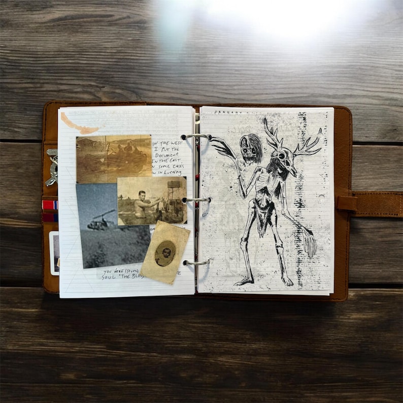 May include: Open leather-bound journal with a drawing of a skeletal figure with antlers and a skull head. The left page has vintage photos and handwritten text. The journal is open on a wooden surface.