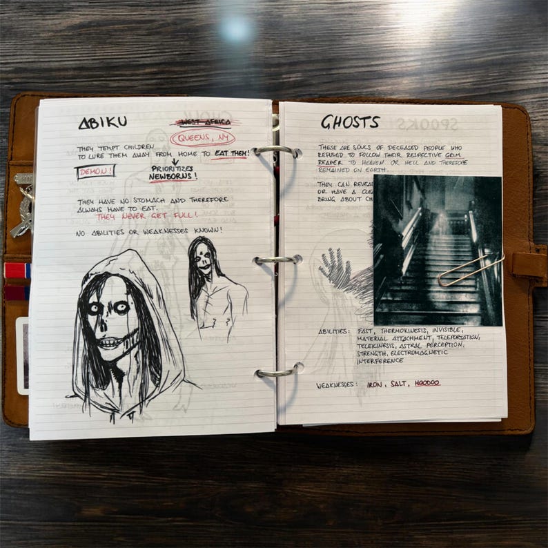 May include: Open notebook with handwritten notes and sketches. The left page details "Abiku" with a drawing of a hooded figure. The right page discusses "Ghosts" with a photo of a staircase and a drawing of a hand.