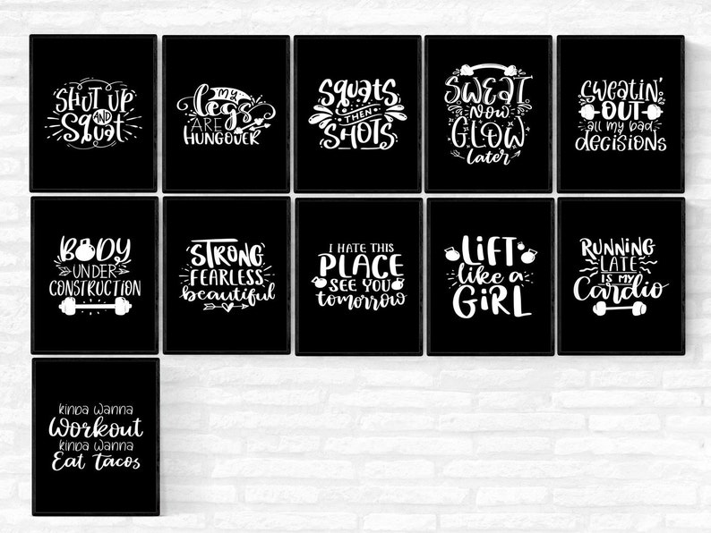 May include: A collection of black framed wall art with white text. The art features motivational phrases related to fitness, such as "Shut up and squat", "My legs are hungover", and "Lift like a girl". The overall theme is fitness and workout.