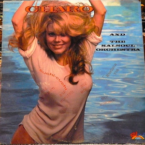 May include: Album cover featuring Charo with the text "Charo" in an orange font. She is wearing a white t-shirt with the words "cuchi-cuchi" and "Bill Morganti" printed on it. The background is a blue water scene with the text "And The Salsoul Orchestra".