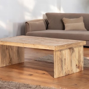 Può includere: Un tavolino da caffè in legno chiaro con un piano rettangolare e un design semplice e moderno. Il tavolo ha una finitura in legno naturale ed è sostenuto da due gambe rettangolari spesse.