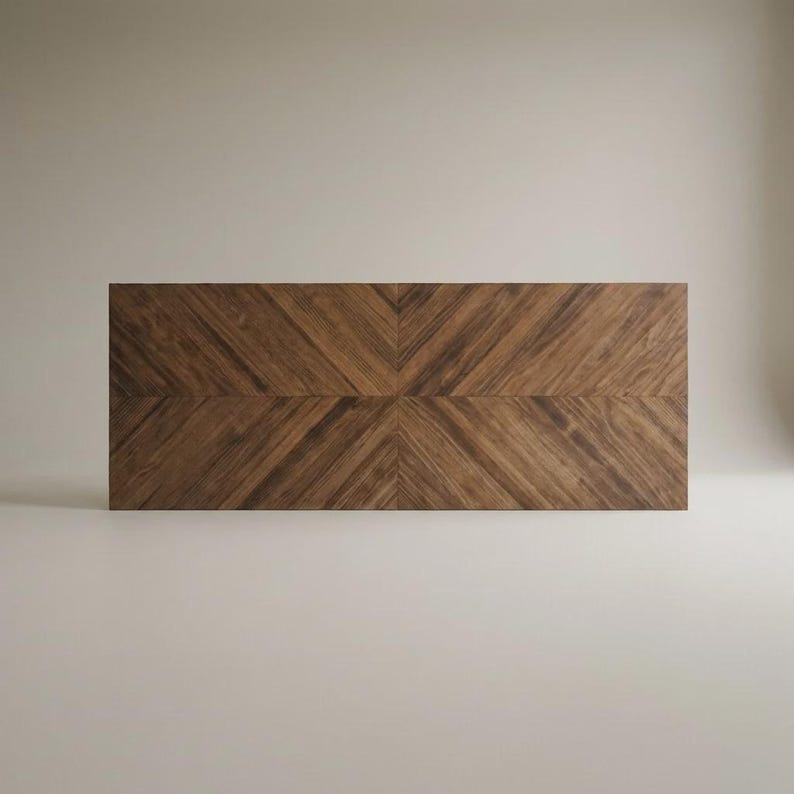 May include: A rectangular wooden tabletop featuring a dark brown walnut grain with a symmetrical chevron pattern. The wood planks are arranged in diagonal lines that meet at a central seam, creating a distinct V-shaped design across the surface.