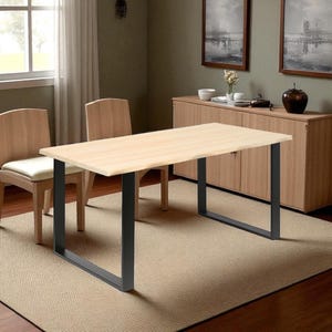Peut inclure: Une table à manger en bois clair avec des pieds en métal noir. Deux chaises en bois avec des coussins crème sont placées près de la table. La table est posée sur un tapis beige dans une pièce avec une fenêtre et des œuvres d'art.