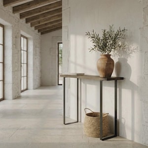Peut inclure: Une console rectangulaire avec un plateau en bois foncé et un cadre en métal noir. Un grand vase en céramique marron clair contenant des branches d'olivier vertes est posé sur la table. Un panier tressé rond et beige est posé au sol.