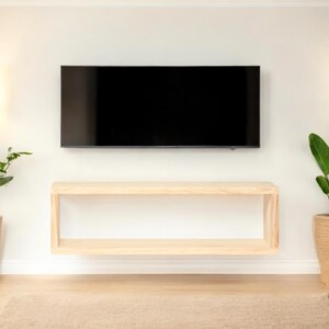 Peut inclure: Aménagement de salon moderne avec une grande télévision à écran plat noire fixée au mur blanc. En dessous, une étagère flottante en bois clair. Des plantes en pot encadrent la télévision, ajoutant une touche de verdure à l'espace.