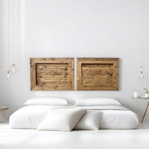 Op de afbeelding: Een wit bed met een wit dekbed en twee witte kussens. Het hoofdbord is gemaakt van twee houten panelen met een rustieke afwerking.
