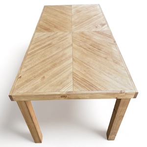 May include: A rectangular wooden table with a light brown finish. The tabletop features a chevron pattern, and the legs are angled for support. The table is approximately 60 inches long and 30 inches wide, suitable for dining or display.