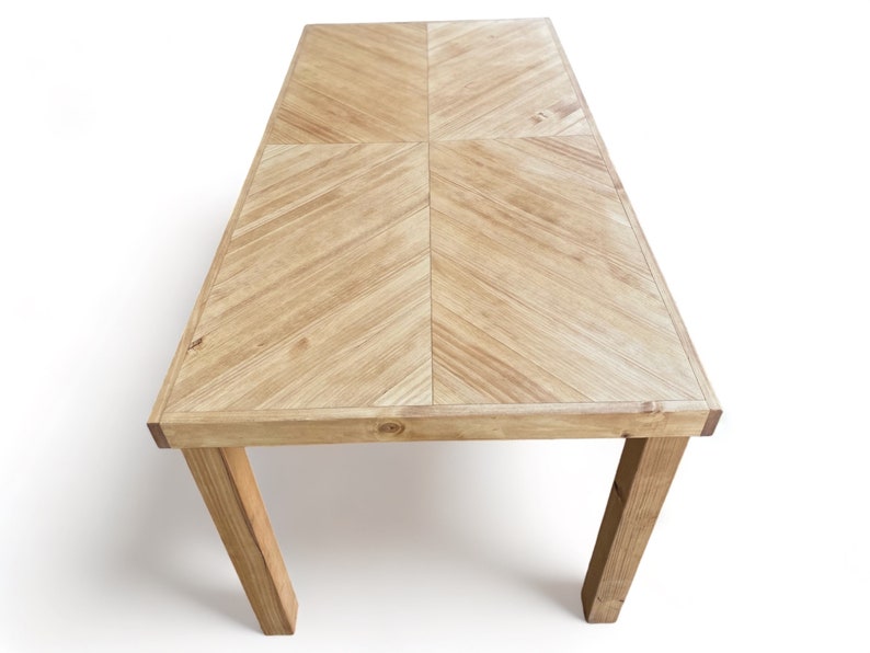 May include: A rectangular wooden table with a light brown finish. The tabletop features a chevron pattern, and the legs are angled for support. The table is approximately 60 inches long and 30 inches wide, suitable for dining or display.