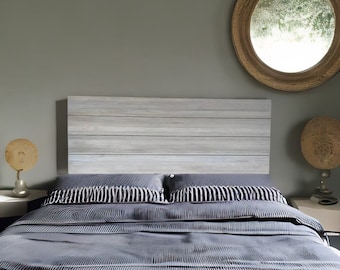 May include: A whitewashed wood headboard with a gray and white striped bedspread on a bed with a gray wall in the background.