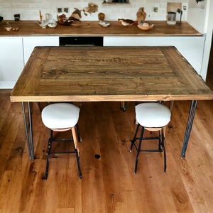 Könnte beinhalten: Ein rechteckiger Holztisch mit dunkelbraunem Finish, getragen von schwarzen Metall-Haarnadelbeinen. Zwei Hocker mit weißer Sitzfläche und schwarzen Rahmen sind unter dem Tisch positioniert. Der Tisch ist etwa 122 cm lang und 91 cm breit.