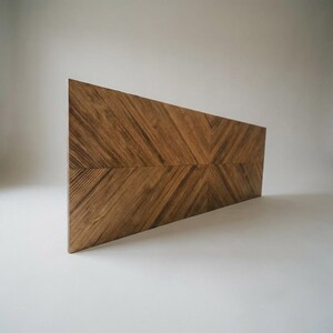 May include: A rectangular wooden panel featuring a prominent chevron pattern created by the arrangement of wood grain. The surface displays a rich brown color with visible natural wood textures and lines running diagonally toward the center.