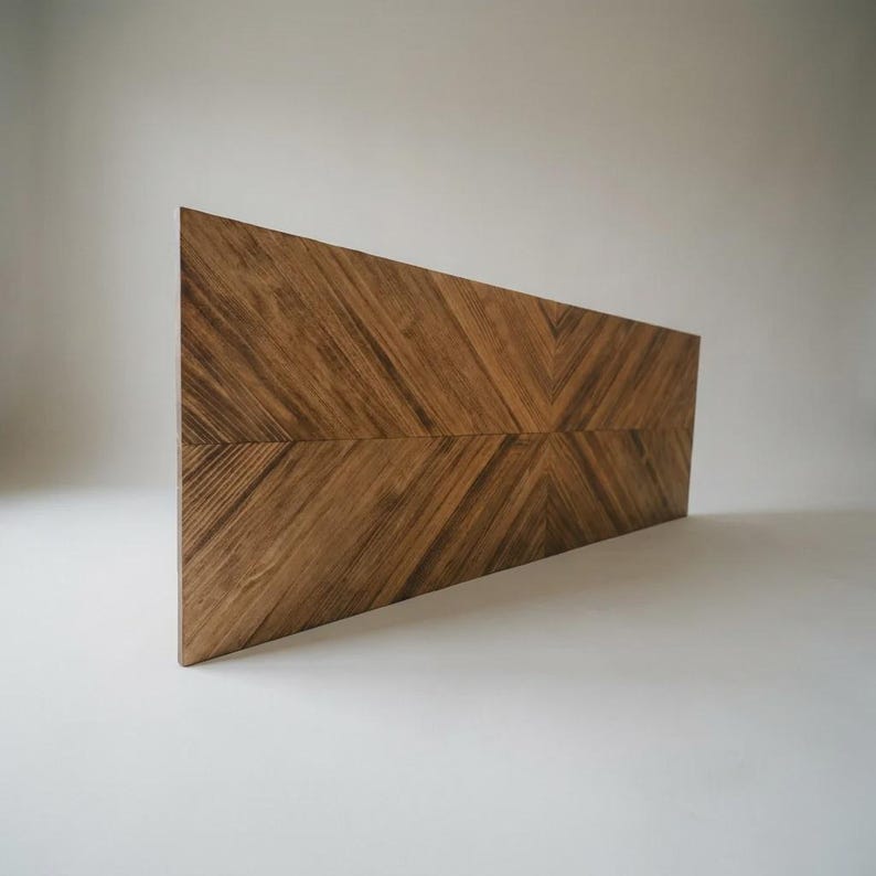 May include: A rectangular wooden panel featuring a prominent chevron pattern created by the arrangement of wood grain. The surface displays a rich brown color with visible natural wood textures and lines running diagonally toward the center.