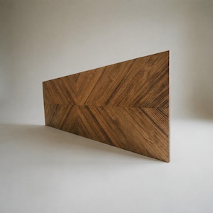 May include: A rectangular wooden panel featuring a prominent chevron pattern created by the arrangement of wood grain. The surface displays a rich medium-brown tone with visible natural wood textures and dark streaks running diagonally across the board.