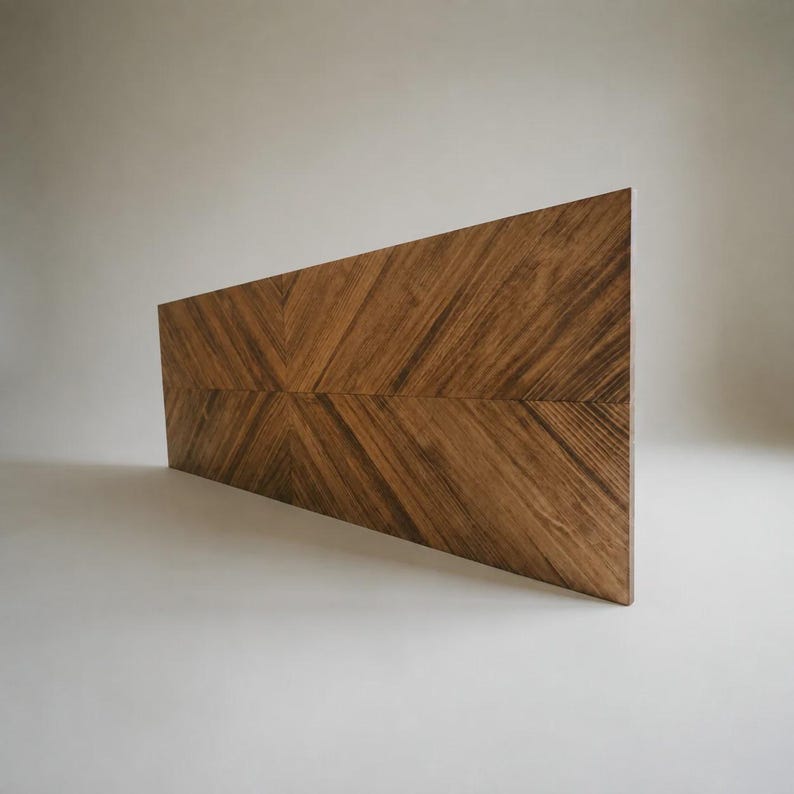 May include: A rectangular wooden panel featuring a prominent chevron pattern created by the arrangement of wood grain. The surface displays a rich medium-brown tone with visible natural wood textures and dark streaks running diagonally across the board.