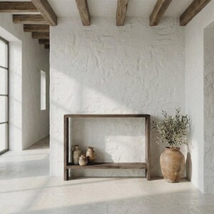 Peut inclure: Une console rectangulaire en bois foncé avec une étagère inférieure, portant deux petits vases en céramique. À côté de la table se trouve un grand pot en terre cuite arrondi contenant un olivier vert aux feuilles fines et branches.