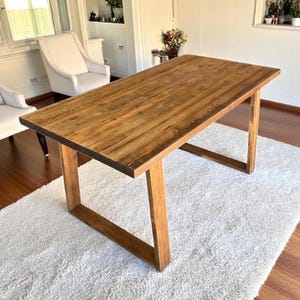 Può includere: Tavolo rettangolare in legno con finitura naturale, sostenuto da gambe angolate. Il tavolo è appoggiato su un tappeto bianco e la stanza presenta sedie bianche e una finestra. Il tavolo misura circa 183 cm di lunghezza.