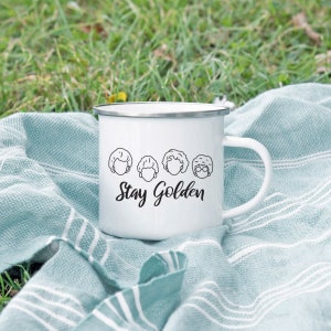 May include: White enamel camping mug with a black outline of four women's faces and the text "Stay Golden".