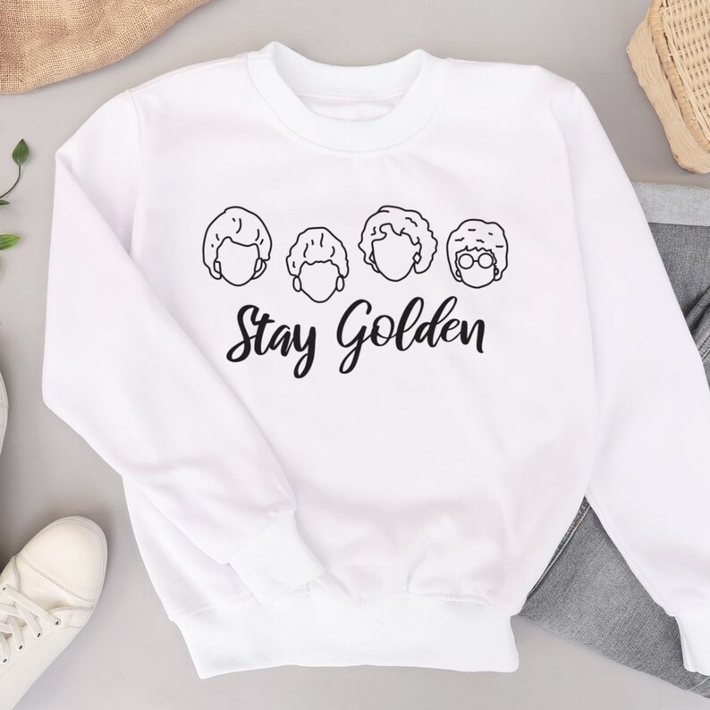 May include: White sweatshirt with a black outline of four women's faces and the text "Stay Golden".