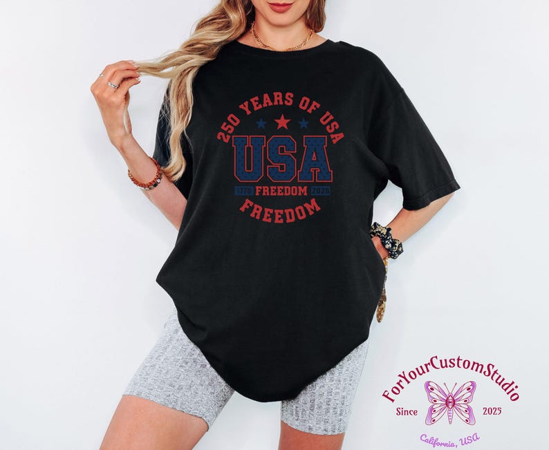 May include: Black t-shirt with a red and blue graphic that reads "250 YEARS OF USA" with "USA" in the center. The shirt also has the words "FREEDOM" printed on it. The shirt is paired with gray shorts. The image also includes the text "ForYourCustomStudio" and "California, USA".
