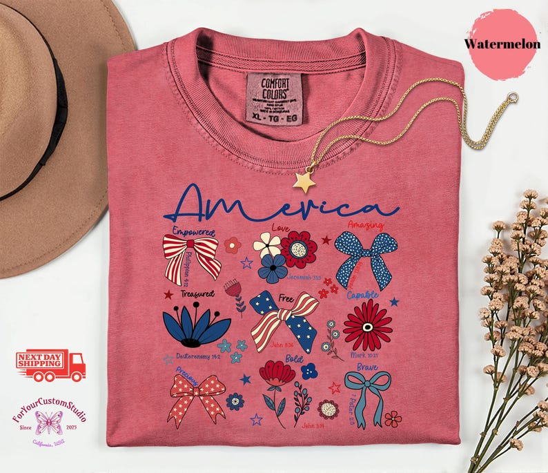 May include: A watermelon-colored t-shirt with the word "America" in blue script. The shirt features patriotic floral and bow designs with words like "Empowered," "Love," and "Free." A gold star necklace is draped across the shirt.
