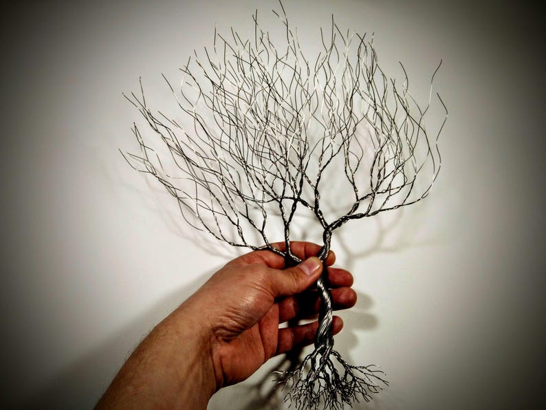 May include: A wire sculpture of a tree with a twisted trunk and intricate branches. The tree is made of silver wire and has a natural, organic look.