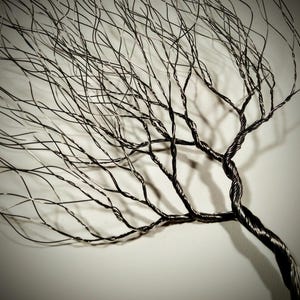 May include: A black wire sculpture of a tree with many branches. The branches are thin and delicate, and they create a sense of movement and growth. The sculpture is made of wire that has been twisted and shaped to create the branches.