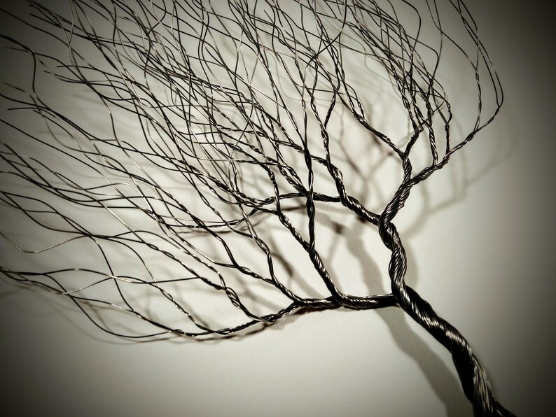 May include: A black wire sculpture of a tree with many branches. The branches are thin and delicate, and they create a sense of movement and growth. The sculpture is made of wire that has been twisted and shaped to create the branches.