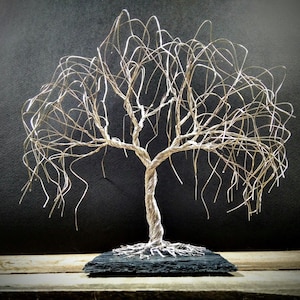 May include: A silver wire sculpture of a weeping willow tree with a black wooden base. The tree is made of thin, twisted wire that creates a realistic weeping willow effect.