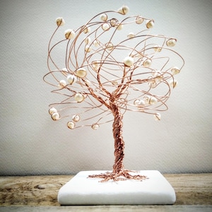 May include: A copper wire sculpture of a tree with white pearl-like beads for leaves. The tree is on a white square base.